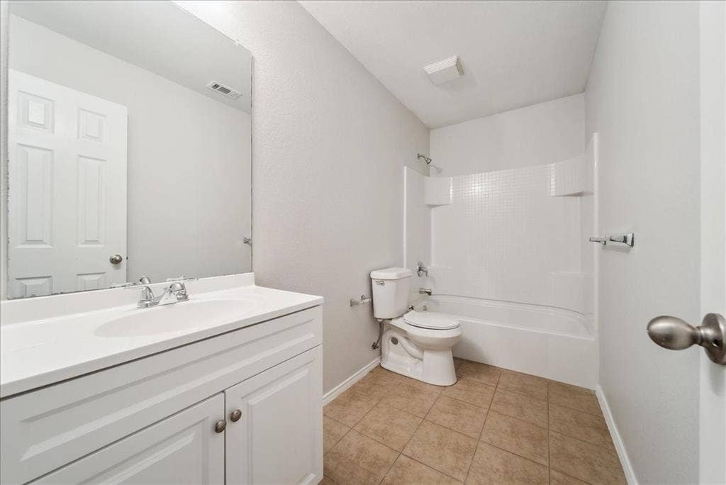 White vanity with integrated sink, chrome faucet, wall-mounted mirror, and tile flooring