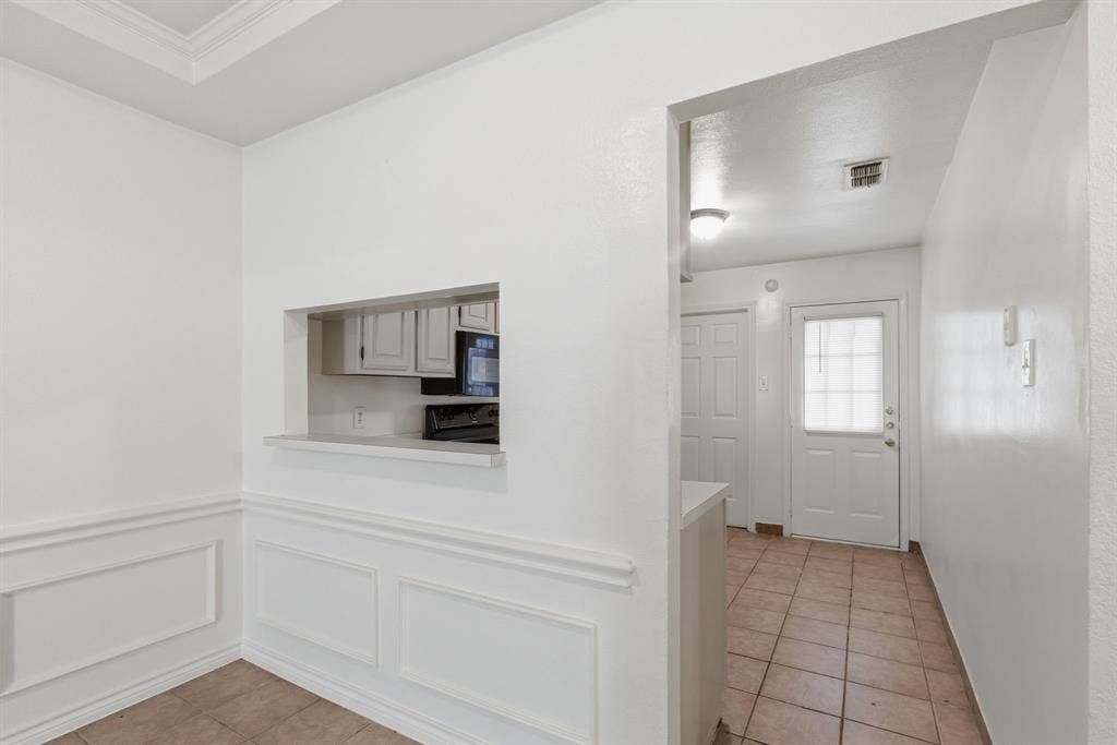 Pass-through window with counter, built-in wall paneling, crown molding, and tiled flooring