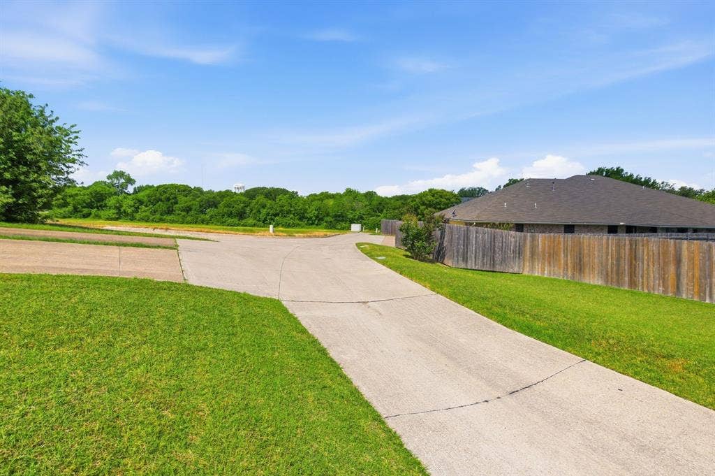 Manicured lawn, concrete driveway, wood privacy fence, and mature trees