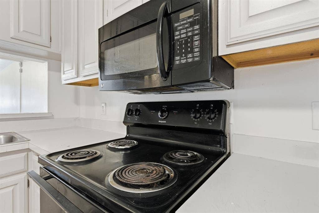 White paneled cabinetry, white countertops, black oven, and black microwave