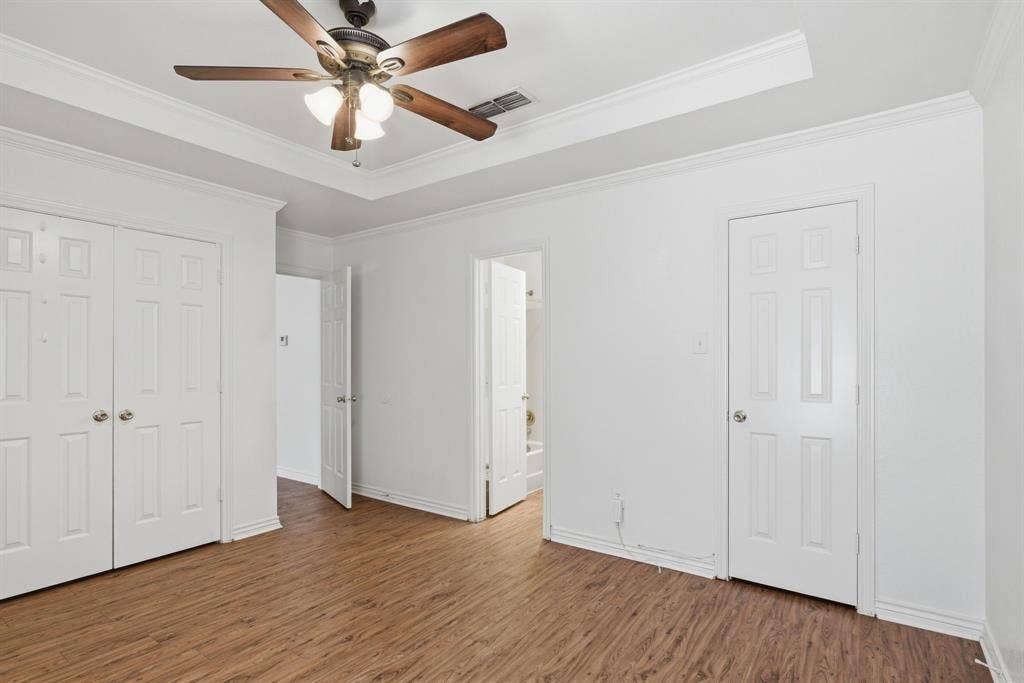 Tray ceiling with crown molding and a ceiling fan, wood-finish flooring, and white paneled doors