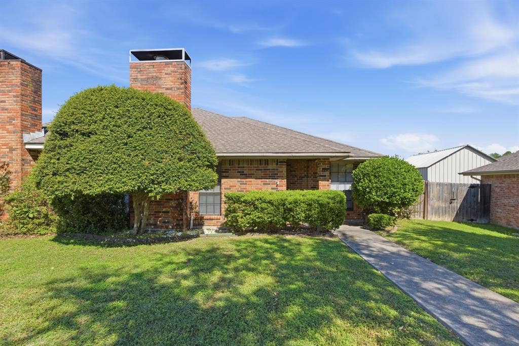 Brick exterior with a shingled roof, two prominent brick chimneys, and a concrete walkway