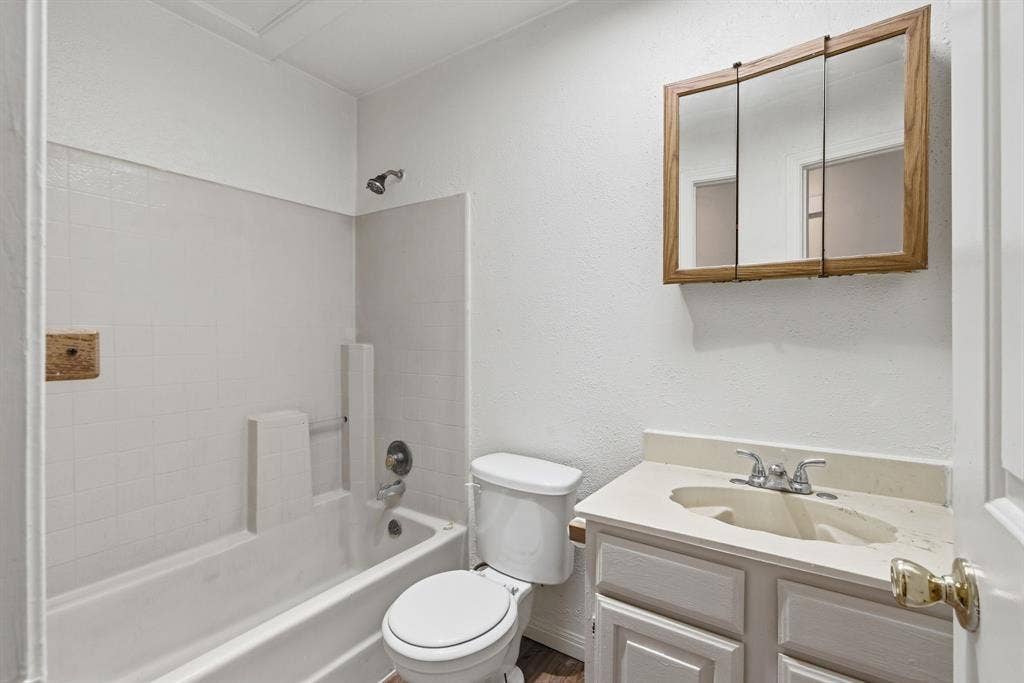 Bathroom featuring a white bathtub with tile surround, a toilet, a vanity with a light-colored countertop, and a wood-framed medicine cabinet