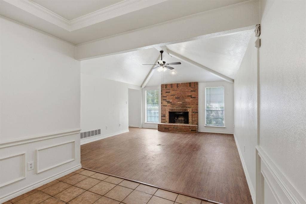 Vaulted ceiling with exposed beams, brick fireplace, wood-finish flooring, and a ceiling fan