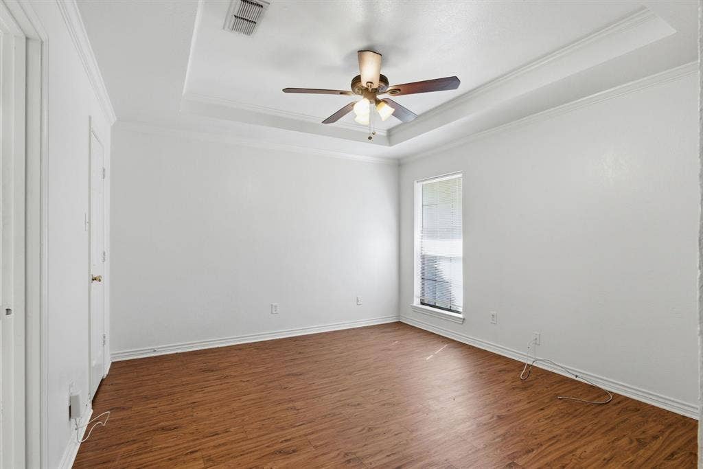 Tray ceiling with crown molding, wood-finish flooring, ceiling fan with light kit, and a single window with blinds