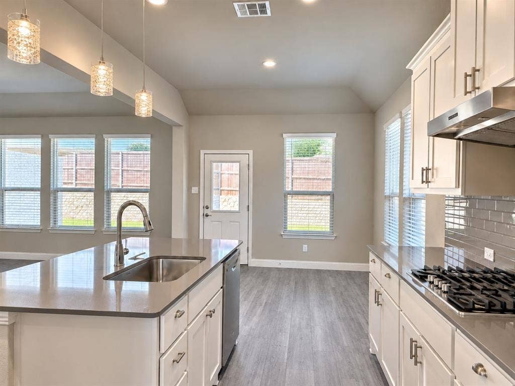 Kitchen featuring a stainless steel sink, gas cooktop, white cabinetry, integrated dishwasher, and pendant lighting