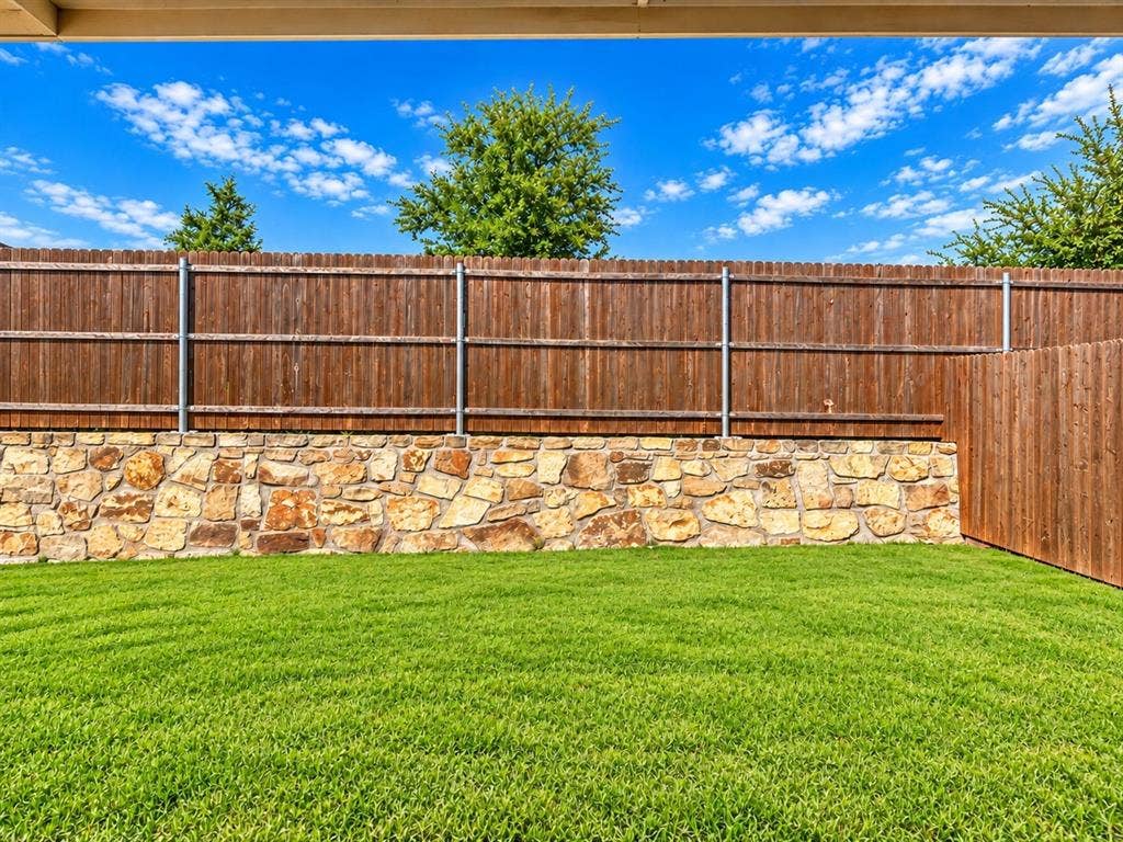 Expansive backyard showcasing a manicured lawn, stone retaining wall, and sturdy wood-finish fencing with metal frame reinforcement
