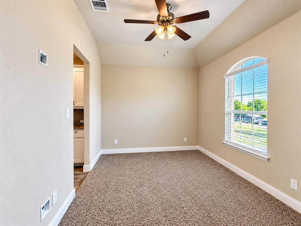 Spacious bedroom featuring neutral wall finishes, plush carpet flooring, arched window with natural light, ceiling fan with integrated lighting, and direct access to an ensuite bathroom