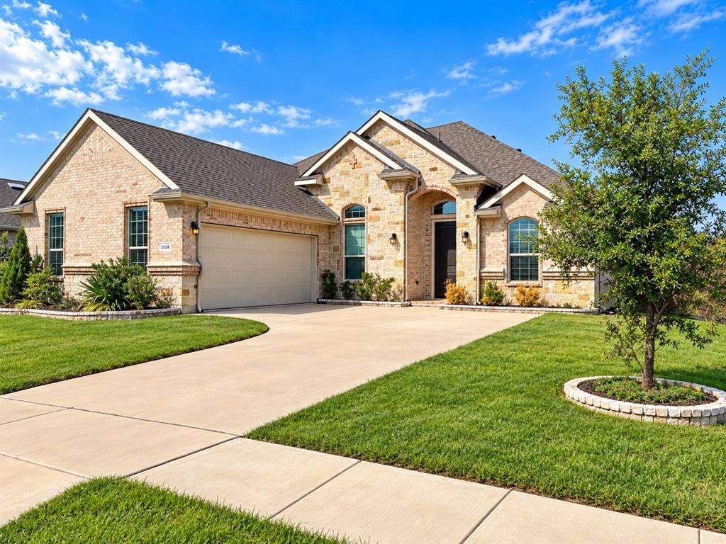 Light brick exterior with stone accents, a dark shingle roof, arched entryway, and a two-car garage