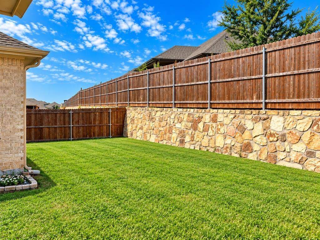 Expansive backyard featuring a lush, manicured lawn bordered by a composite wood-finish fence with white trim and a stone retaining wall