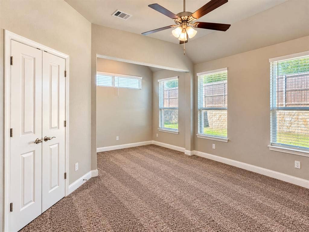 Vaulted ceiling with a ceiling fan, three large windows, textured carpeting, and double-door closet