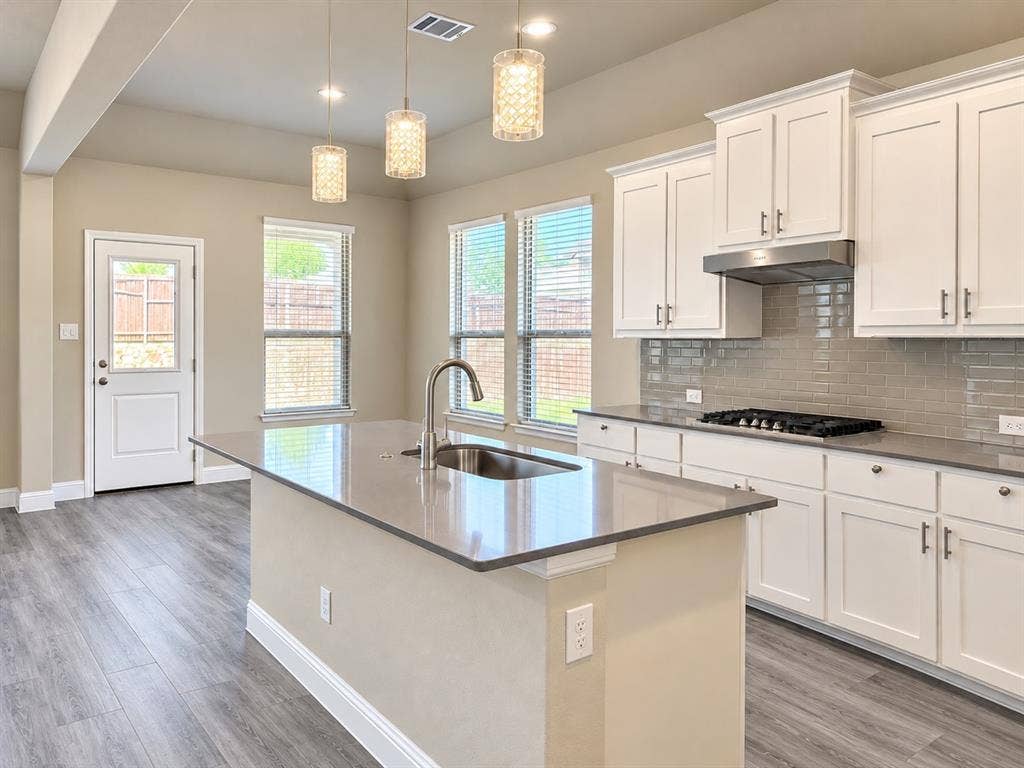 Kitchen featuring an island with a stainless steel sink, wood-finish flooring, white cabinetry, a gas range, and a subway tile backsplash