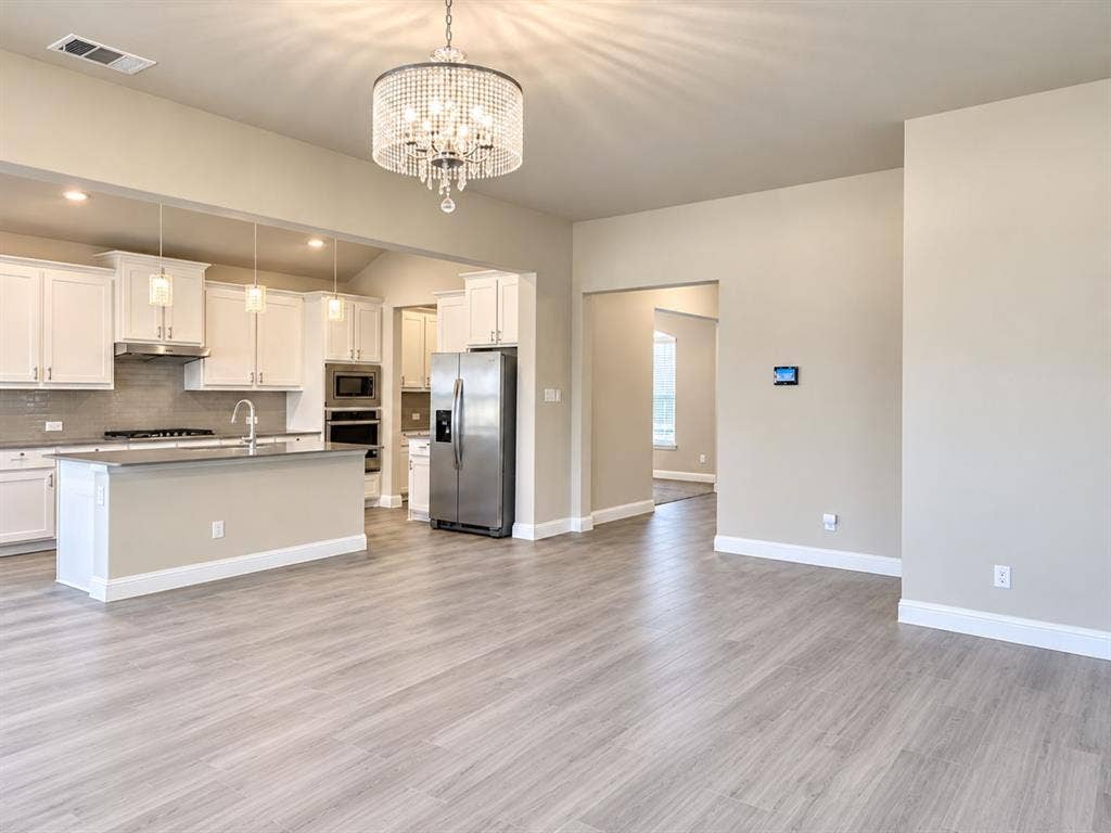 Spacious open-concept living area with wood-finish flooring, a contemporary chandelier, and recessed lighting