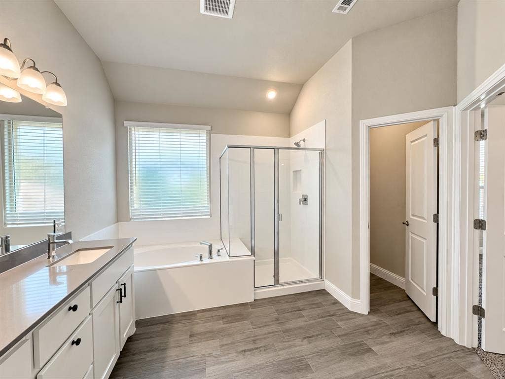 Bathroom featuring a double vanity with stone countertops, a soaking tub, a glass-enclosed shower, and wood-finish flooring