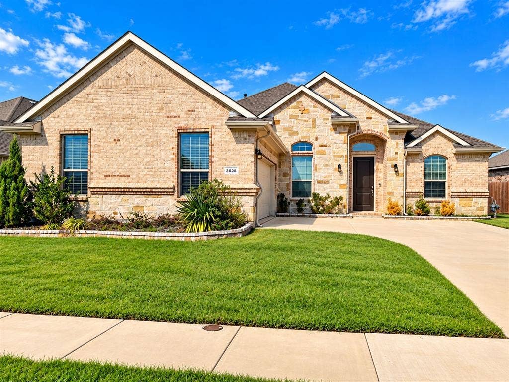 Elegant brick exterior with multiple arched windows and transom details, complemented by a professionally landscaped front lawn with mature plantings and defined hardscape borders