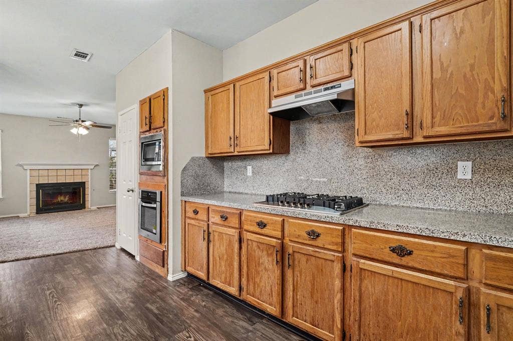 Open floorplan: View of stained kitchen cabinets, gas drop-in gas cooktop, wall oven and microwave opened to the family room.