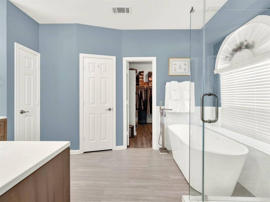 A freestanding tub sits beneath a tall window, its curved silhouette softened by filtered daylight and pale tile. Slip into a warm bath after a busy day and enjoy a little time to yourself. Also, get a peek into the HUGE walk-in closet.