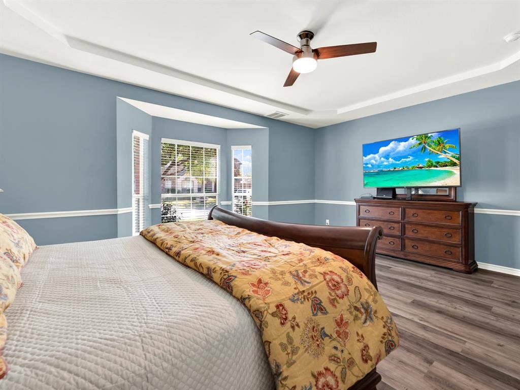 Soft blue walls and white chair rail frame a sunlit bay window, creating a perfect reading spot within the spacious primary bedroom. Settle in with a good book and enjoy a quiet afternoon with views of the trees outside.
