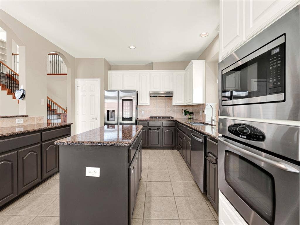 White upper cabinets and deep gray lower cabinetry frame the stainless steel appliances, giving the kitchen a crisp, layered look. Try a new recipe on the gas cooktop while something delicious bakes in the nearby wall oven.