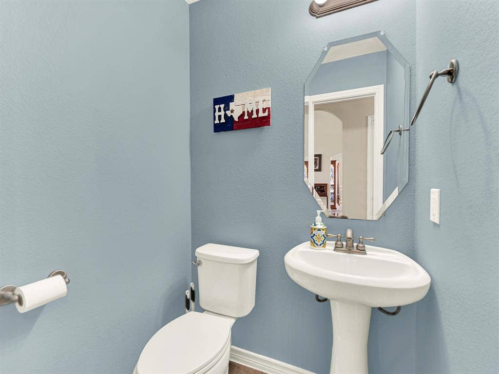 A sculpted pedestal sink keeps the powder room feeling open, while a beveled mirror reflects light against pale blue walls. Guests can freshen up before returning to the evening’s festivities.