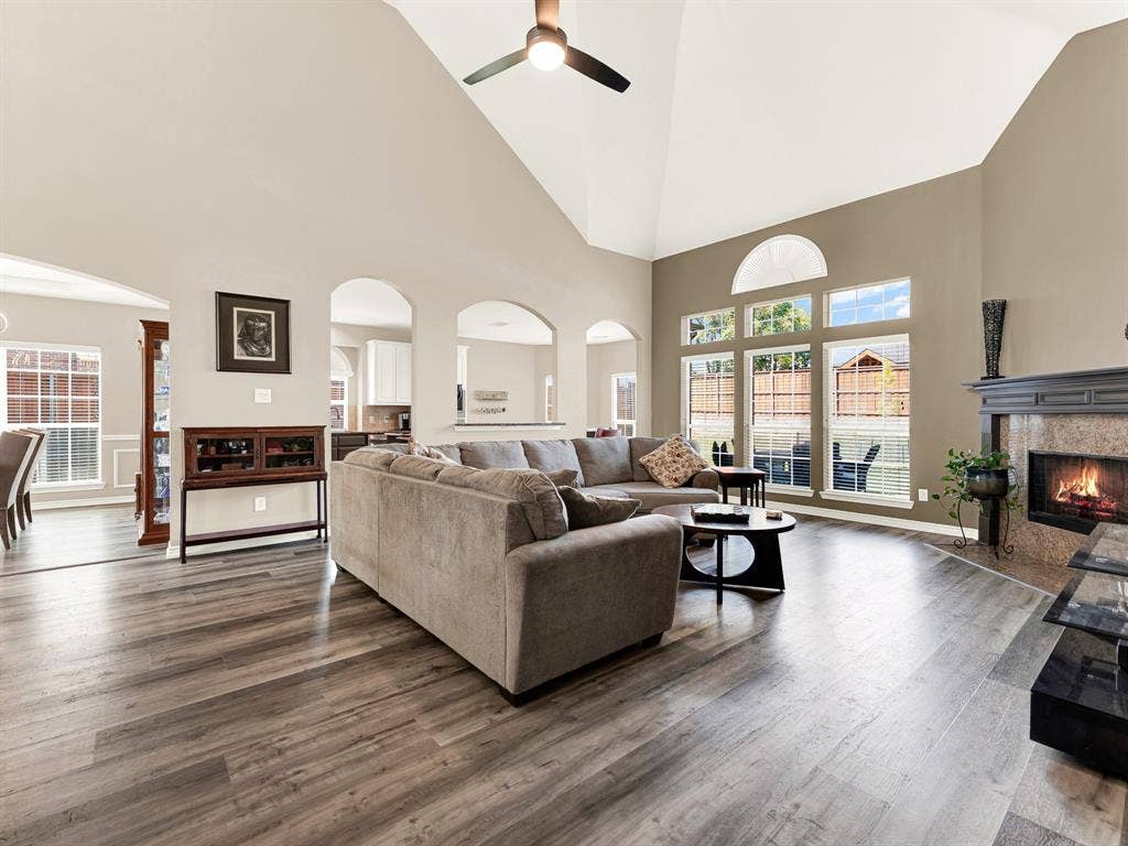 A soaring ceiling and stacked windows fill the living room with daylight, highlighting the grain of the new laminate flooring. Spend a leisurely afternoon here sharing stories while the backyard stays in view.