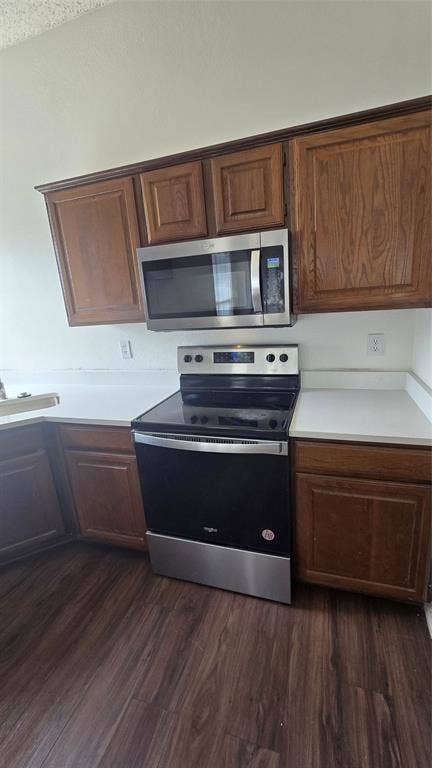 Hardwood-finish flooring, white countertops, built-in wooden cabinetry, stainless steel microwave, and a stainless steel oven range