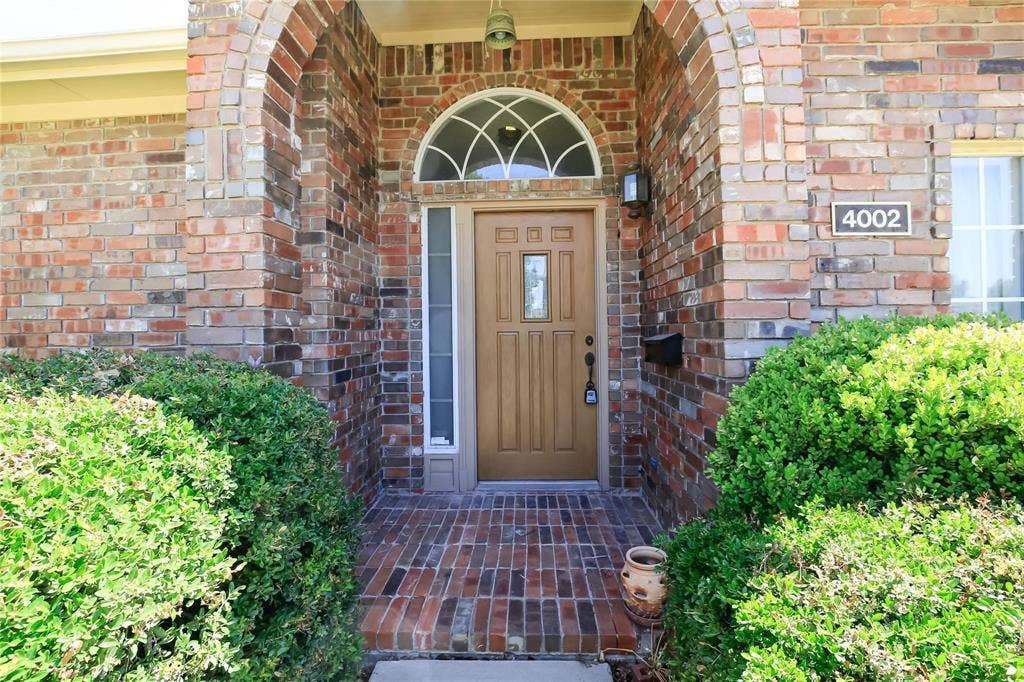 Brick facade with an arched entry, a light wood-finish door, and a decorative transom window