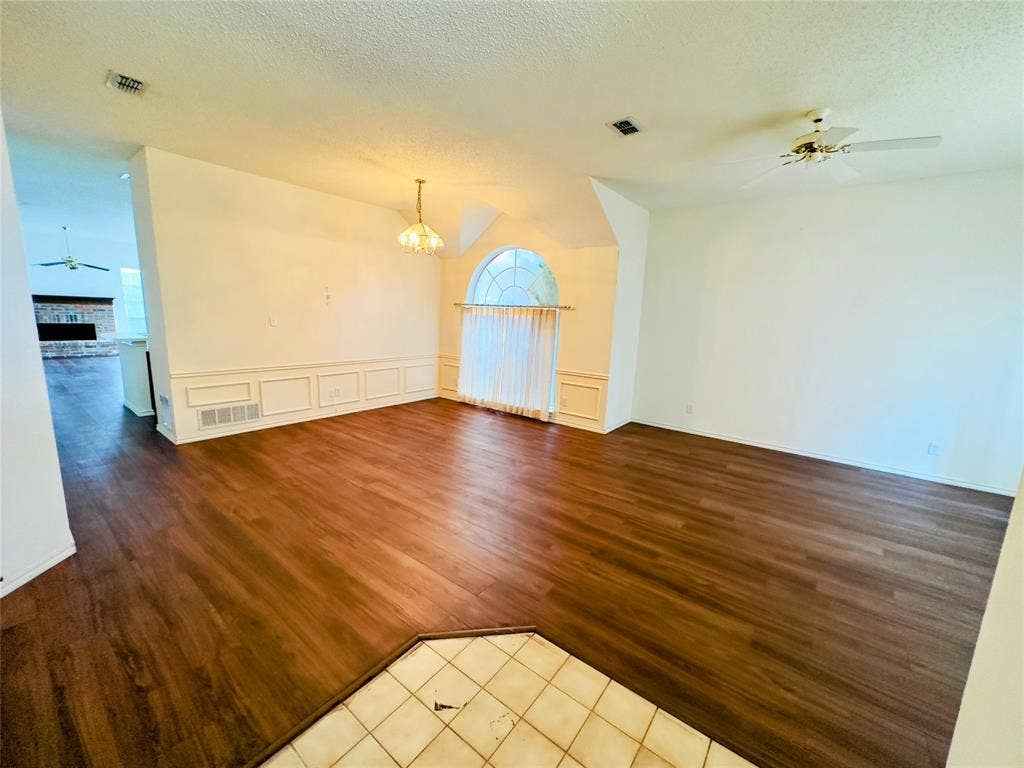 Wood-finish flooring throughout, decorative wainscoting, an arched window, and a ceiling fan