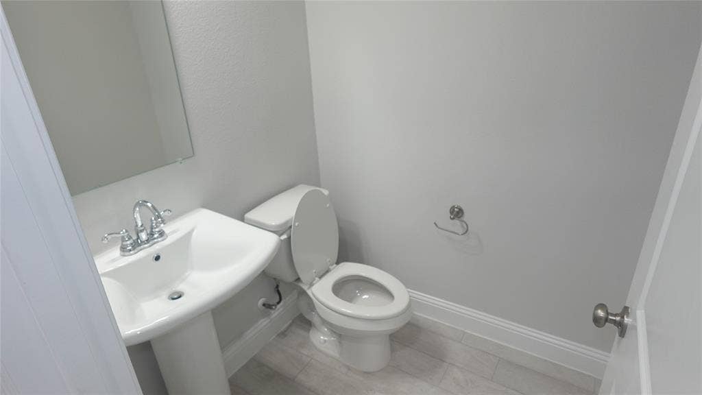 Pedestal sink with chrome faucet, wall-mounted mirror, ceramic tile flooring, and a white commode