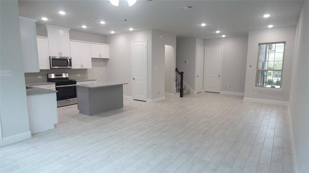 Open-concept living space with light wood-finish flooring, recessed lighting, and a kitchen featuring white cabinetry, stainless steel appliances, and a central island