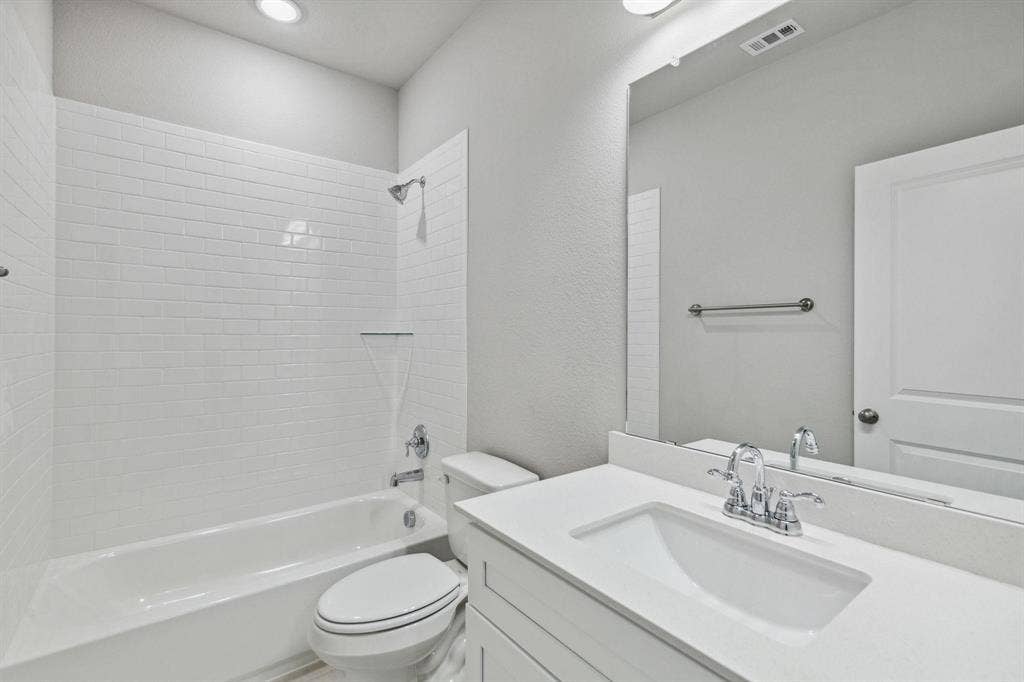 Bathroom featuring a white subway tile shower surround, a built-in tub, a white vanity with an integrated sink, a large wall-mounted mirror, and overhead lighting