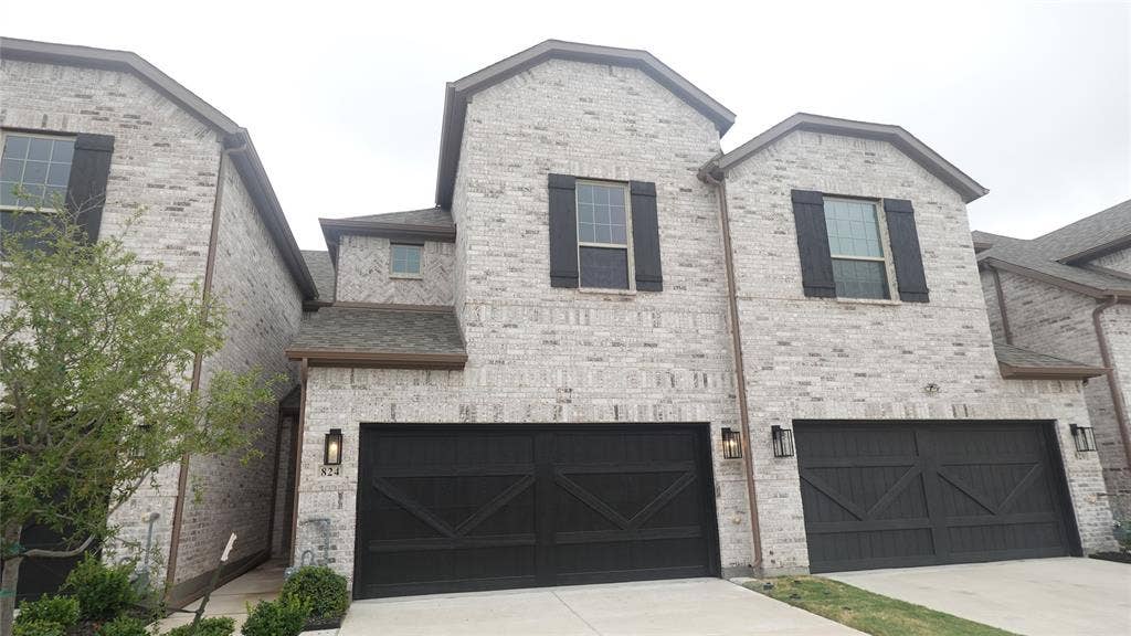 Brick exterior with dark shutters, dark garage doors, and a gabled roofline