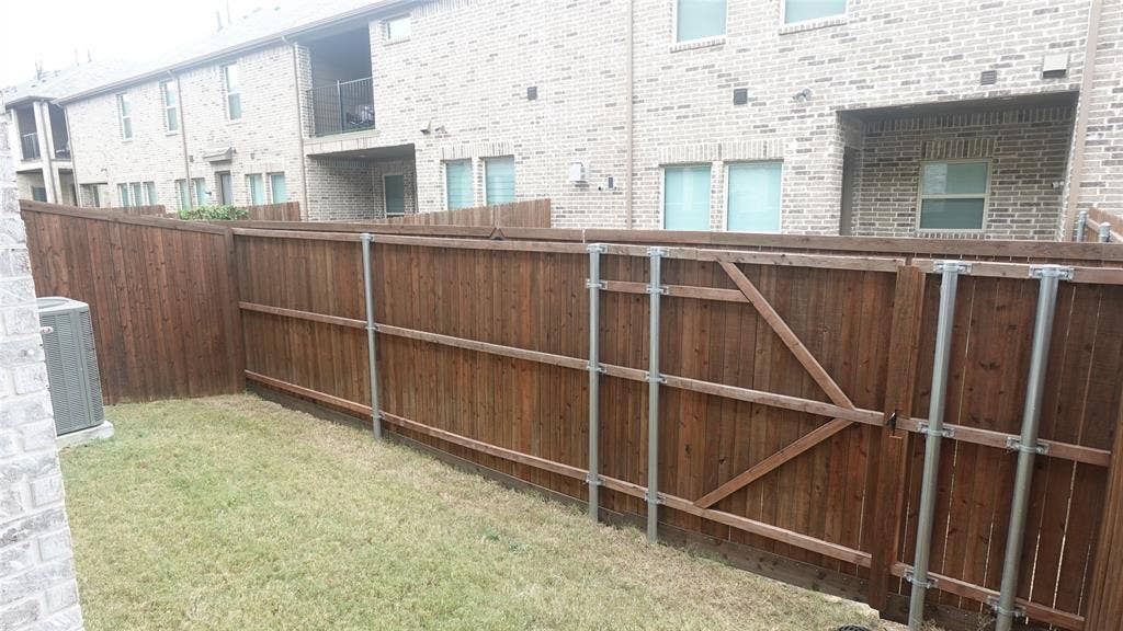 Enclosed outdoor space featuring a wood-panel fence with metal posts, a gate with diagonal bracing, and a grass lawn