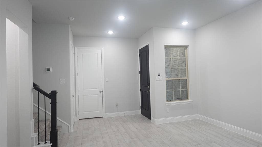 Recessed lighting illuminates wood-finish flooring, a contemporary window, and a dark paneled door