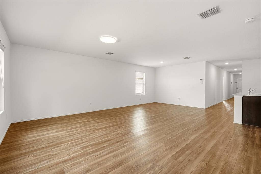 Expansive room with light wood-finish flooring, white walls, and a single window