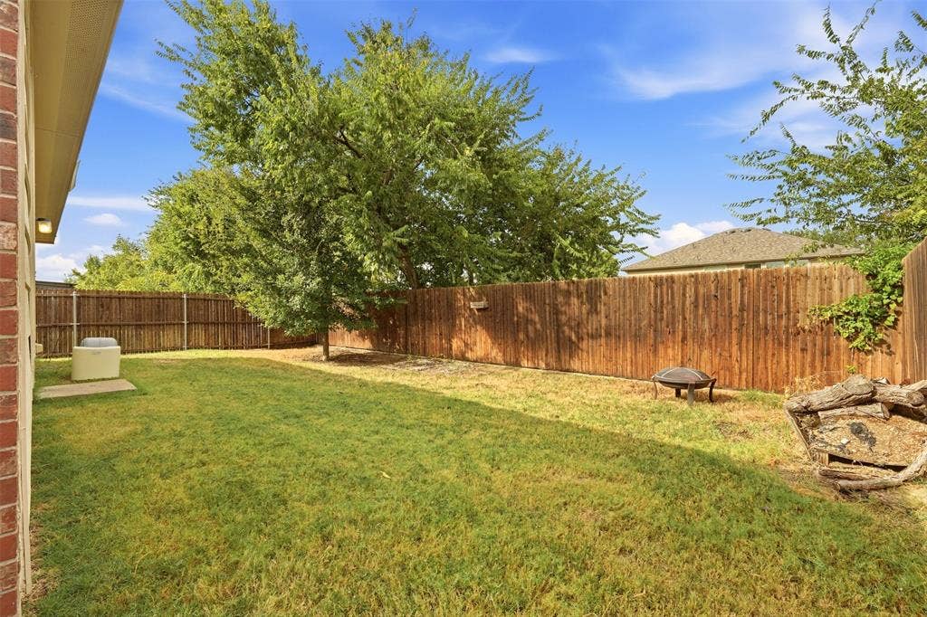 Fenced backyard featuring a lawn and mature trees