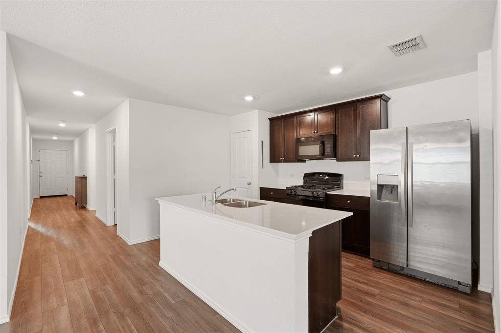Open-concept kitchen featuring an island with an undermount sink, stainless steel appliances, dark wood cabinetry, and wood-finish flooring