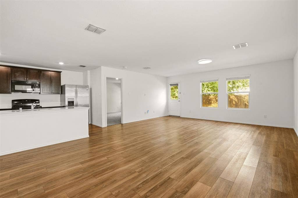 Open-concept living space featuring wood-finish flooring, white walls, recessed lighting, and a kitchen with dark wood cabinetry and stainless steel appliances