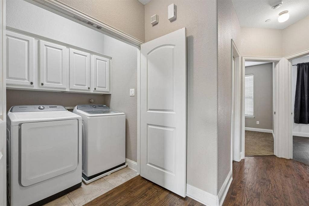 Laundry area featuring white cabinetry with dark hardware and light-toned tile flooring