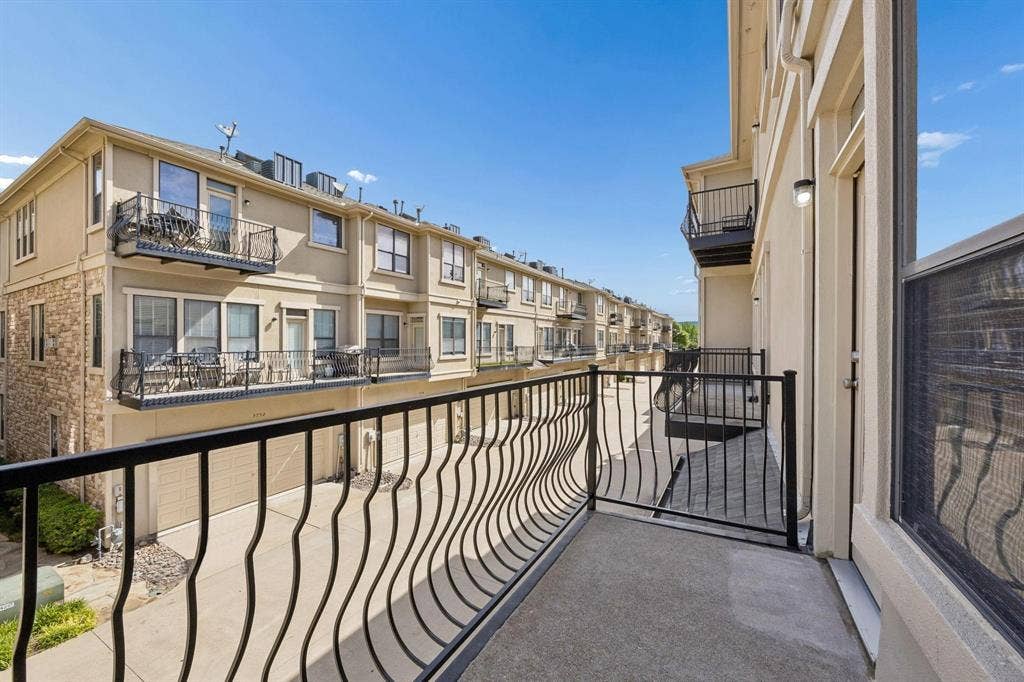 Private balcony with black wrought iron railing, concrete flooring, and an exterior wall-mounted light fixture