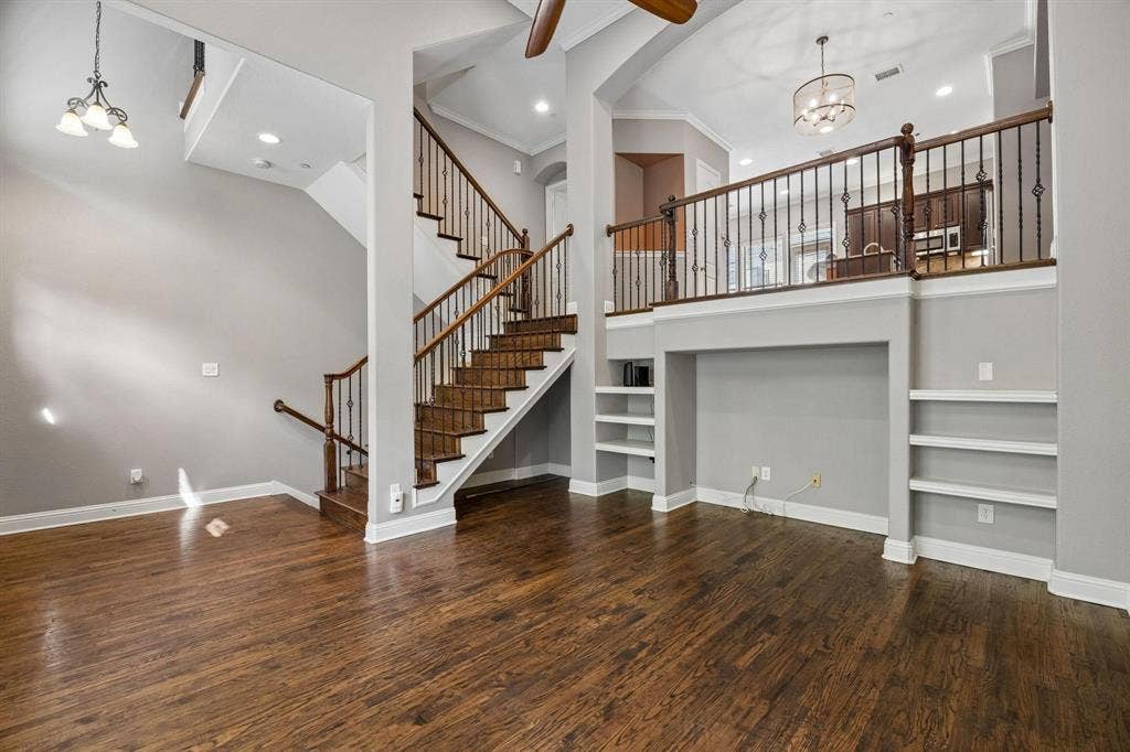 Wood-finish flooring with a multi-level layout, featuring an open staircase with decorative metal balusters, integrated shelving, and recessed lighting