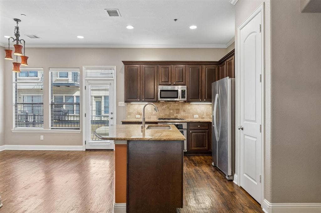Kitchen featuring dark wood cabinetry, stainless steel appliances, a granite countertop island with an undermount sink, and wood-finish flooring