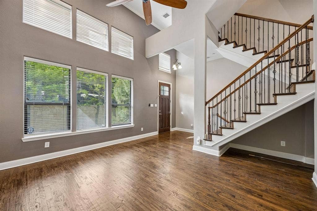 Vaulted ceiling with a ceiling fan, wood-finish flooring, multiple windows, staircase with wrought iron balusters, and a solid wood entry door