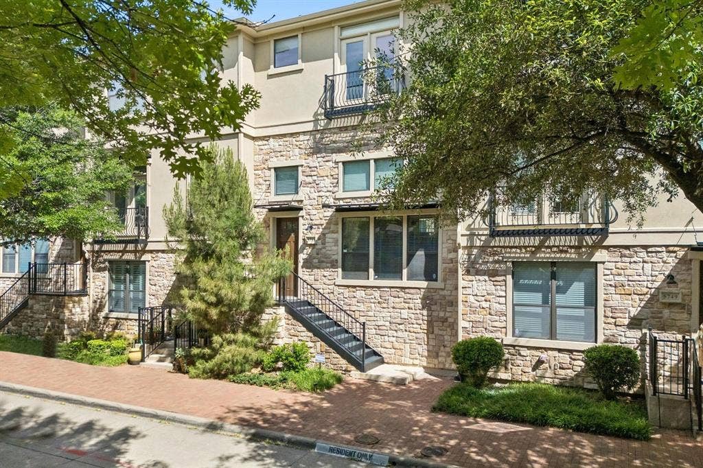 Stone and stucco facade with black metal railings, front entry staircase, and mature landscaping
