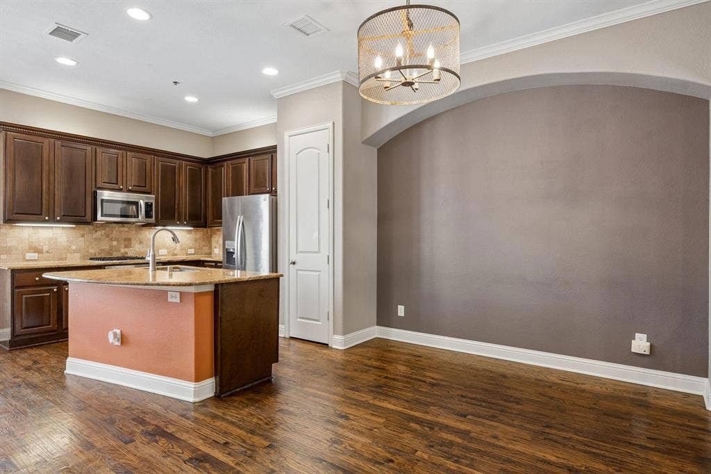Kitchen featuring dark wood cabinetry, stainless steel appliances, a center island with sink, and wood-finish flooring