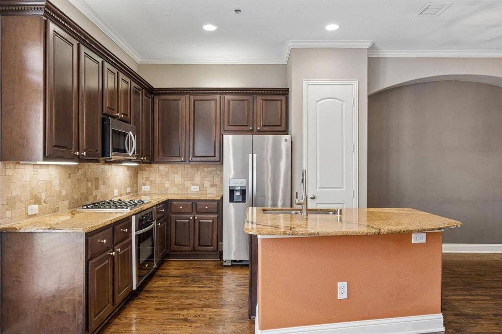 Kitchen featuring dark wood cabinetry, stainless steel appliances, granite countertops, and a tiled backsplash