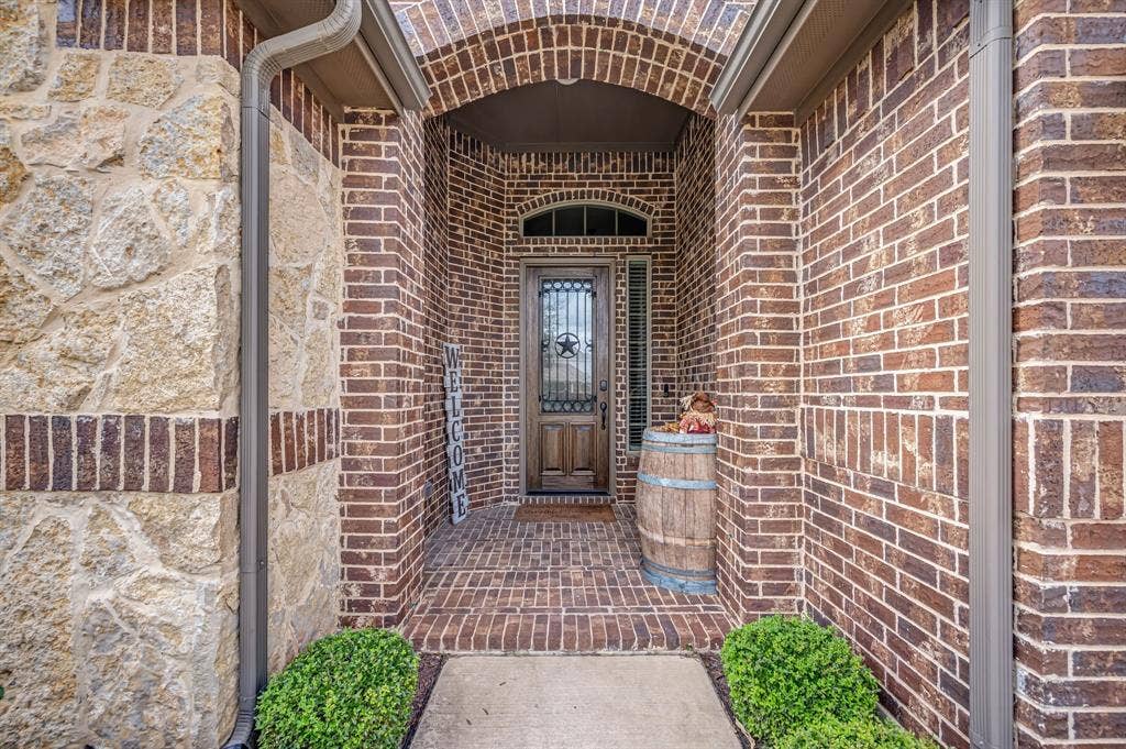 Brick exterior facade featuring a stone veneer accent, arched entryway, and a solid wood front door with decorative metal insert