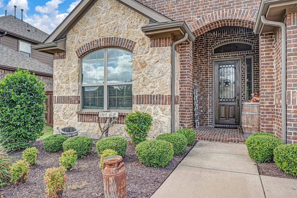 Exterior facade featuring textured stone veneer and brick masonry, arched entryway with a decorative iron-insert door, and concrete walkway
