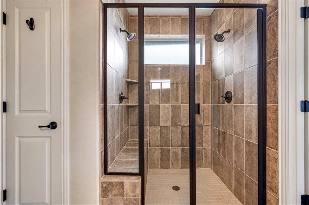 Walk-in shower featuring floor-to-ceiling tile, a built-in tiled bench, dual showerheads with matte black fixtures, and a framed glass enclosure