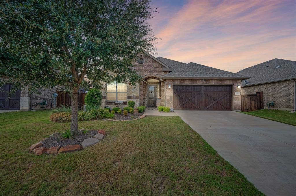 Brick exterior with decorative wood-finish garage doors, stone-bordered landscaping, and paved driveway